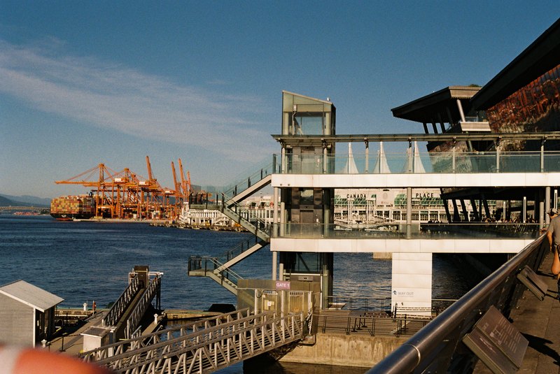 Waterfront stairs and buildings with orange cargo cranes across the harbor.