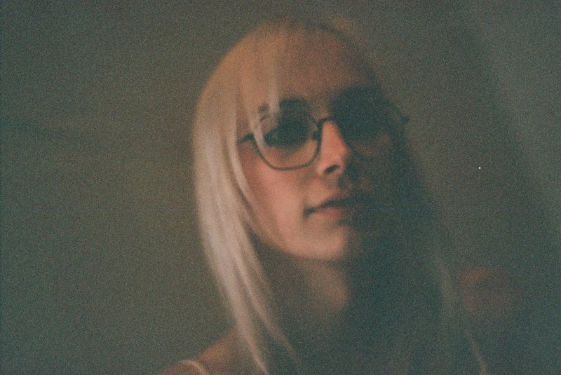 A grainy portrait of a person wearing glasses in low light.