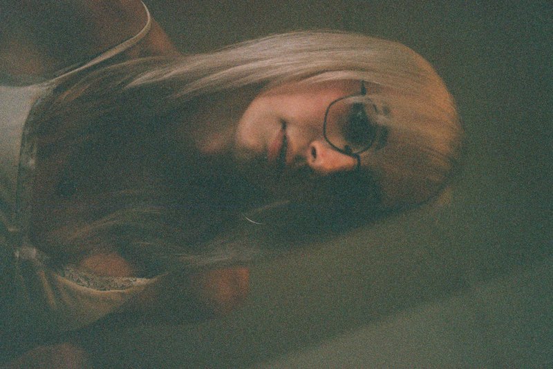 A grainy vertical portrait of a person with glasses in low light.