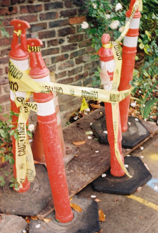 Orange traffic posts wrapped in caution tape beside a brick wall.