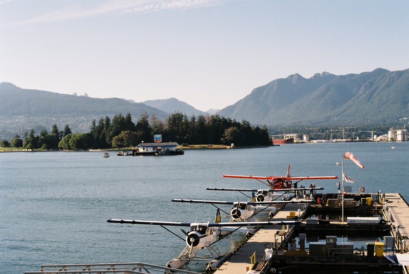 Seaplanes lined up at a dock with water and mountains beyond.